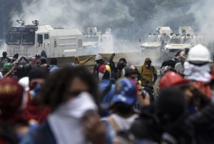 Opposition activists, equipped with helmets, gas masks, makeshift shields and barricaded behind debris, face charging riot police during a protest against Venezuelan President Nicolas Maduro, in Caracas on May 3, 2017. Venezuela's angry opposition rallied Wednesday vowing huge street protests against President Nicolas Maduro's plan to rewrite the constitution and accusing him of dodging elections to cling to power despite deadly unrest. / AFP PHOTO / JUAN BARRETO