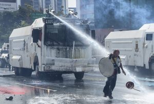 An opposition activist is hit at close quarters by the jet from a riot police water cannon during a protest against President Nicolas Maduro in Caracas, on May 10, 2017. Venezuelan protesters hit the streets on Wednesday armed with "Poopootov cocktails," jars filled with excrement which they vowed to hurl at police as a wave of anti-government demonstrations turned dirty. / AFP PHOTO / JUAN BARRETO