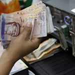 A cashier counts Venezuelan bolivar notes in a state-run supermarket in Caracas