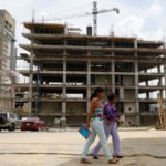 Women walk in front of a building under construction in Caracas