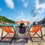 Woman with hat sitting on chairs beach in beautiful tropical bea
