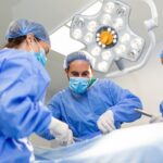 Surgeons doing surgery in operating theatre. Male and female surgeons operating patient. Medical professionals are wearing scrubs.